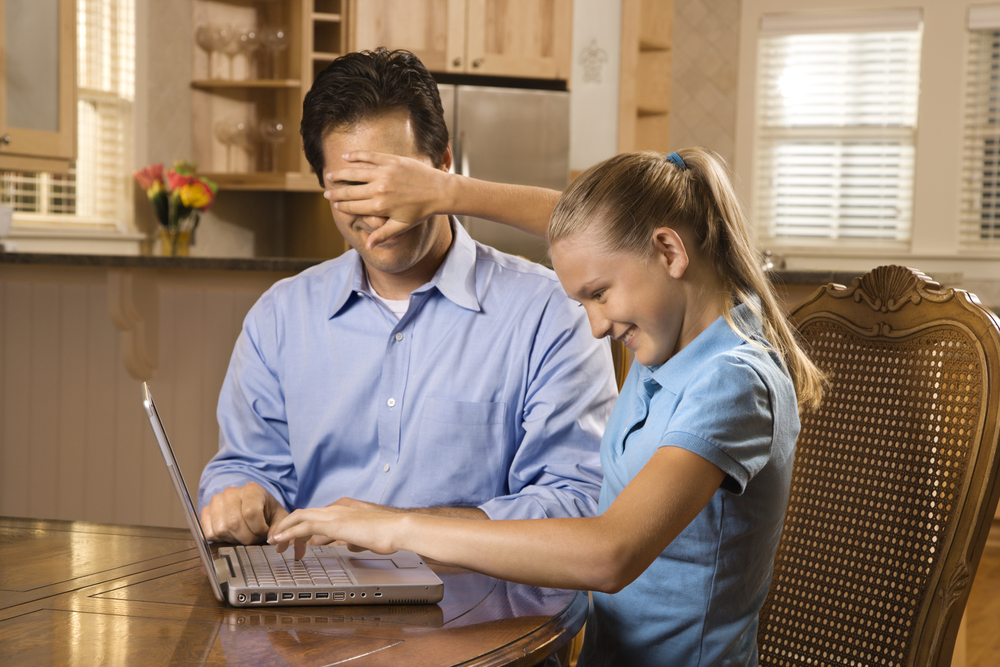 An image of young girl working on laptop at home covering man's face with hand.